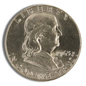 Close-up of a 1963 Franklin half dollar coin featuring the profile of Benjamin Franklin, with inscriptions "LIBERTY" and "IN GOD WE TRUST." The coin's metallic surface displays wear and age, highlighting its historical significance in American numismatics.